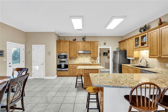 kitchen with sink, light stone countertops, appliances with stainless steel finishes, tasteful backsplash, and a kitchen bar