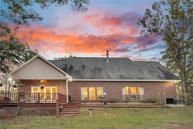 back house at dusk featuring central air condition unit, a deck, and a lawn