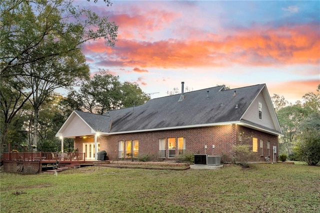 back house at dusk with a wooden deck, a yard, and cooling unit