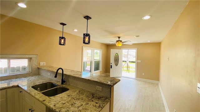 kitchen with sink, light stone counters, hanging light fixtures, kitchen peninsula, and light hardwood / wood-style floors