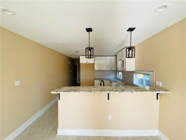 kitchen with white cabinetry, a kitchen breakfast bar, kitchen peninsula, and pendant lighting