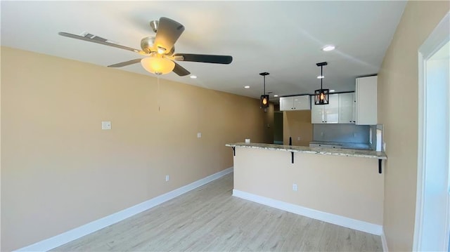 kitchen with a breakfast bar, decorative light fixtures, white cabinets, light stone counters, and kitchen peninsula