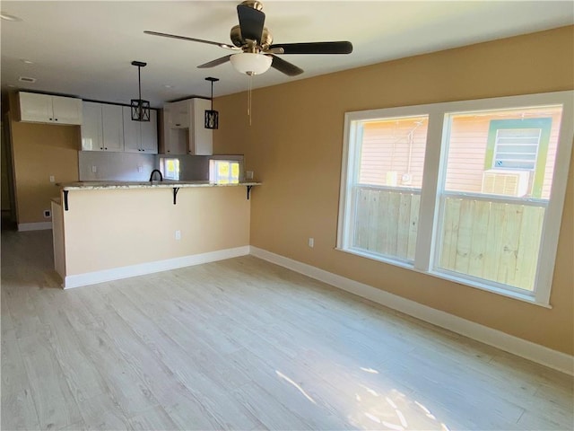 kitchen with decorative light fixtures, white cabinetry, a kitchen breakfast bar, light hardwood / wood-style floors, and kitchen peninsula