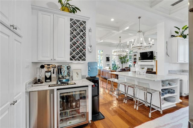 bar with light hardwood / wood-style flooring, white cabinets, decorative light fixtures, and beamed ceiling