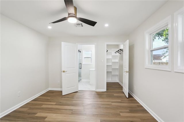 unfurnished bedroom with ceiling fan, dark wood-type flooring, a spacious closet, connected bathroom, and a closet