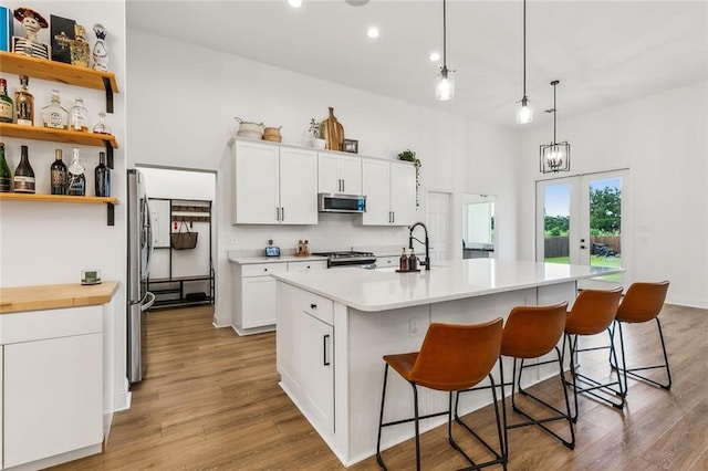 kitchen with appliances with stainless steel finishes, a breakfast bar, pendant lighting, white cabinetry, and a center island with sink