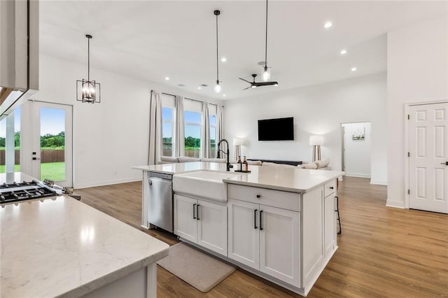 kitchen with pendant lighting, sink, white cabinets, stainless steel dishwasher, and a center island with sink