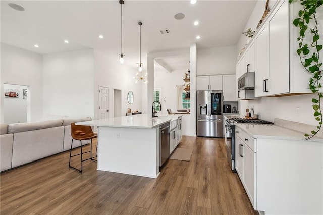 kitchen with appliances with stainless steel finishes, dark hardwood / wood-style floors, pendant lighting, white cabinetry, and a kitchen island with sink