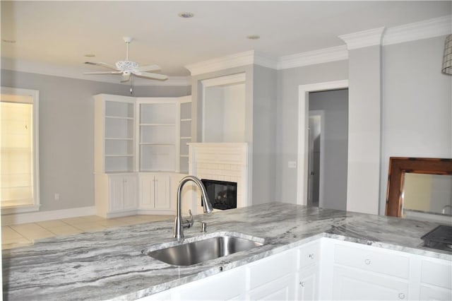 kitchen with light stone countertops, sink, light tile patterned flooring, white cabinets, and ornamental molding