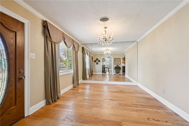 hall featuring a chandelier, a textured ceiling, light wood-type flooring, and crown molding