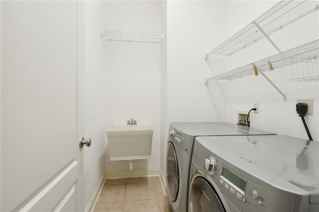 clothes washing area featuring light tile patterned flooring, washing machine and dryer, and sink