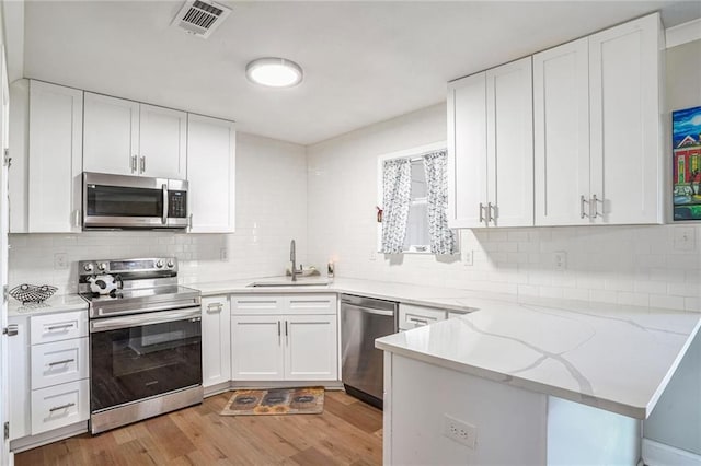 kitchen with light stone countertops, sink, kitchen peninsula, white cabinets, and appliances with stainless steel finishes