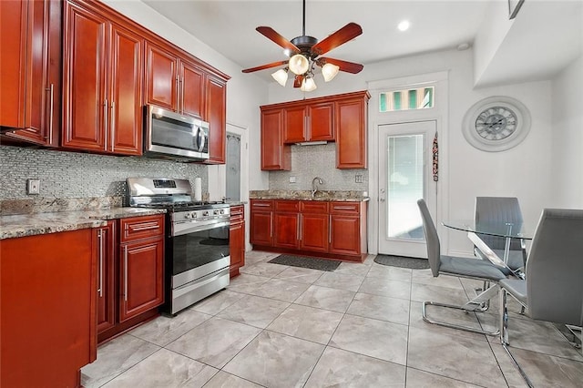 kitchen featuring ceiling fan, sink, light stone countertops, stainless steel appliances, and backsplash