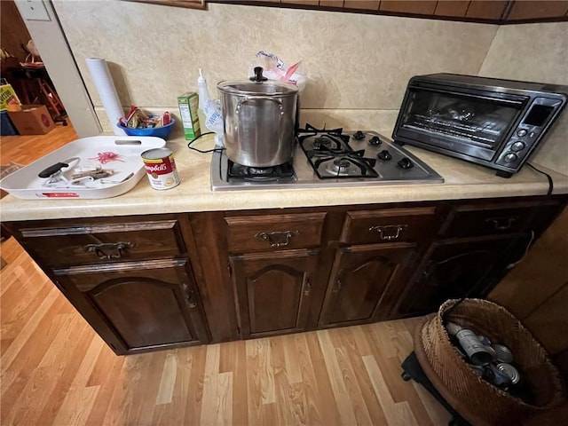 kitchen with stainless steel gas cooktop, dark brown cabinets, and light wood-type flooring