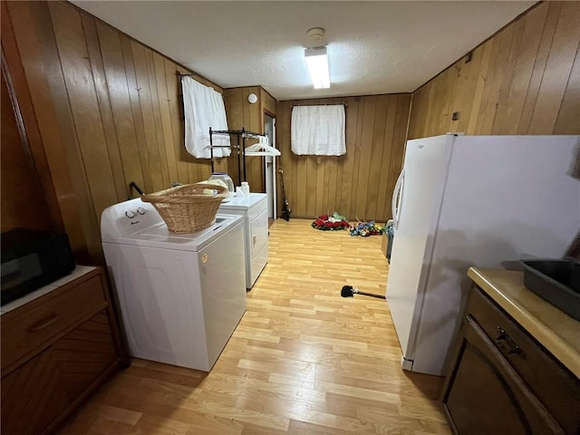 laundry area with washing machine and clothes dryer, a textured ceiling, light hardwood / wood-style floors, and wood walls