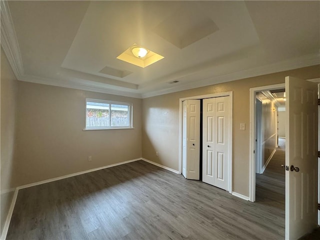 unfurnished bedroom featuring a raised ceiling, dark hardwood / wood-style flooring, ornamental molding, and a closet