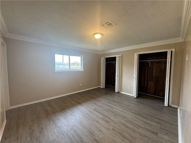 unfurnished bedroom featuring two closets, crown molding, dark hardwood / wood-style flooring, and a textured ceiling