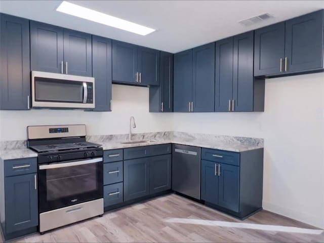 kitchen featuring blue cabinetry, light stone countertops, sink, stainless steel appliances, and light wood-type flooring