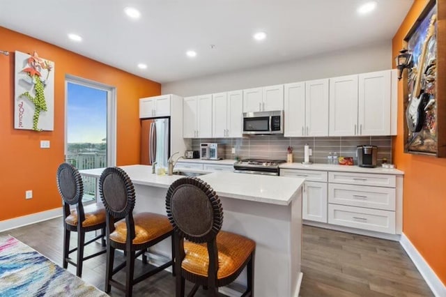 kitchen with appliances with stainless steel finishes, sink, white cabinets, a kitchen breakfast bar, and a center island with sink