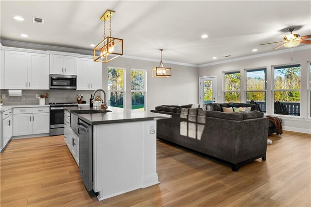 kitchen featuring stainless steel appliances, decorative light fixtures, a center island with sink, white cabinets, and light wood-type flooring