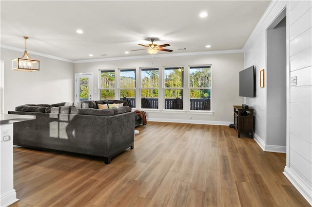 living room with hardwood / wood-style flooring, crown molding, and ceiling fan with notable chandelier