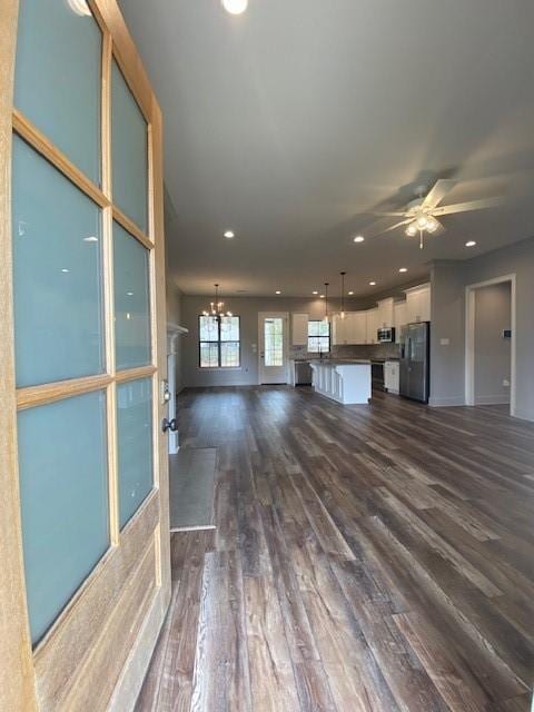 unfurnished living room featuring ceiling fan with notable chandelier and dark wood-type flooring