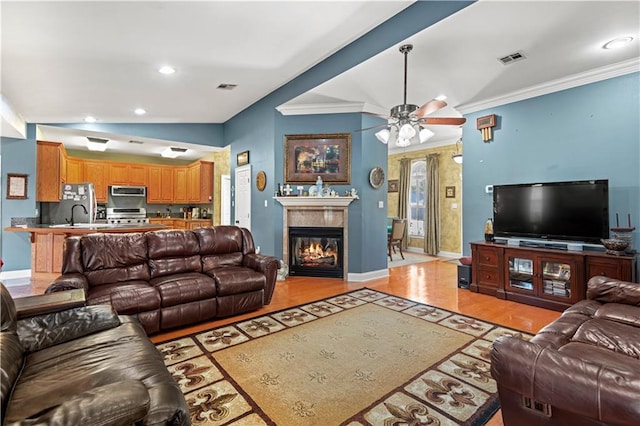 living room featuring ornamental molding, a glass covered fireplace, visible vents, and lofted ceiling