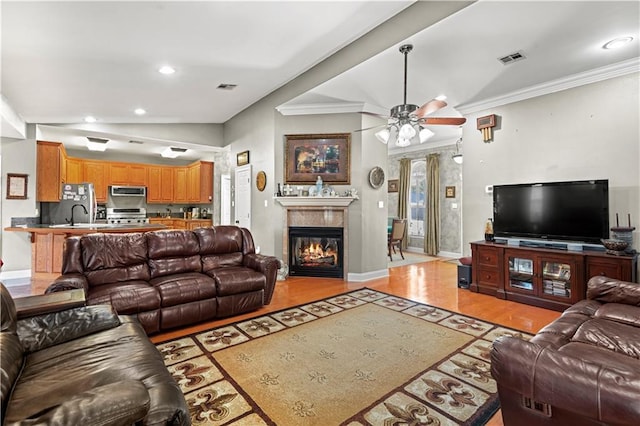 living area with ceiling fan, ornamental molding, a glass covered fireplace, and visible vents