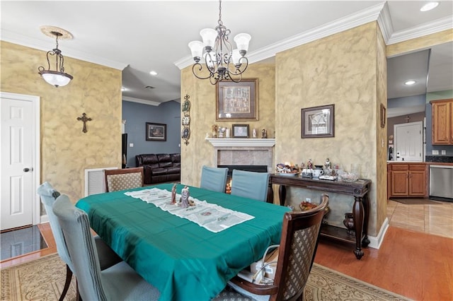 dining area featuring ornamental molding, light wood-type flooring, baseboards, a fireplace, and a notable chandelier