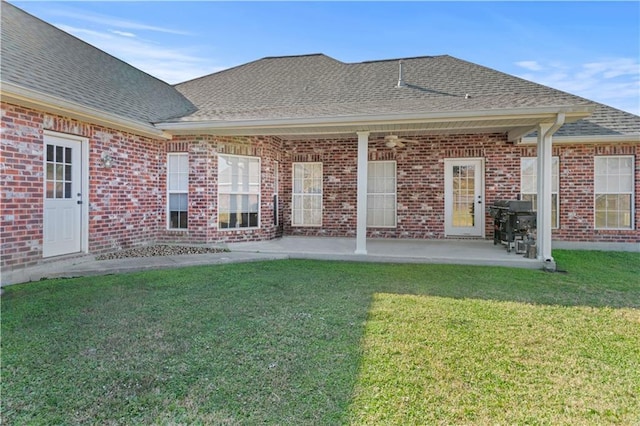 rear view of property featuring a lawn, roof with shingles, a patio area, and brick siding