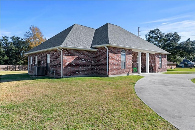 view of side of property featuring a yard, roof with shingles, brick siding, and central AC unit