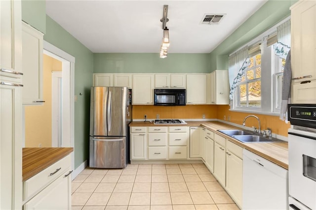 kitchen with appliances with stainless steel finishes, sink, decorative light fixtures, butcher block countertops, and light tile patterned flooring