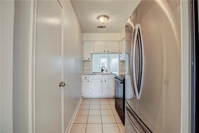 kitchen featuring stainless steel fridge, black range with electric cooktop, sink, white cabinetry, and light tile patterned flooring