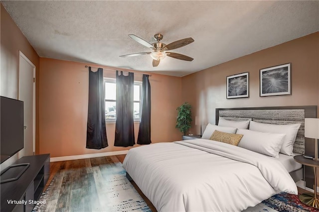 bedroom with a textured ceiling, ceiling fan, and dark wood-type flooring