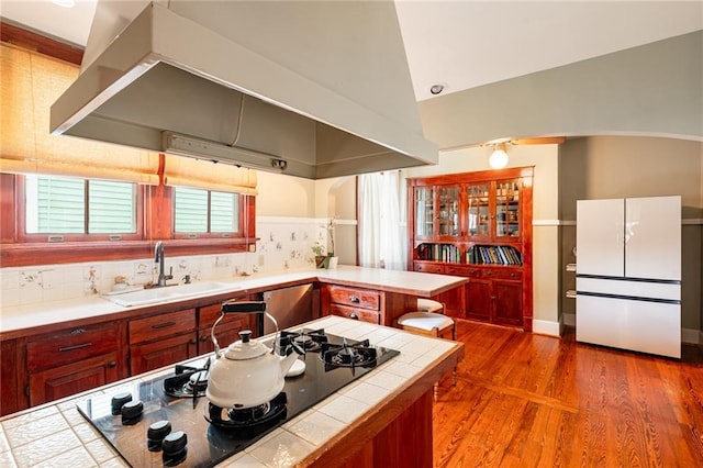 kitchen with sink, tile counters, white refrigerator, lofted ceiling, and black stovetop