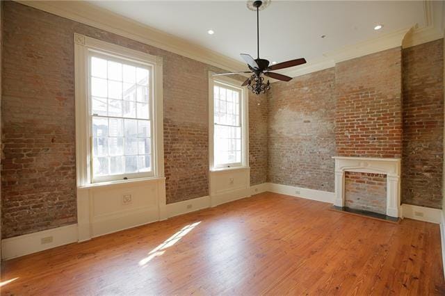 unfurnished living room featuring hardwood / wood-style floors, ceiling fan, crown molding, and brick wall