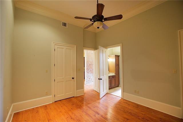 unfurnished bedroom featuring light wood-type flooring, ensuite bath, ceiling fan, and ornamental molding