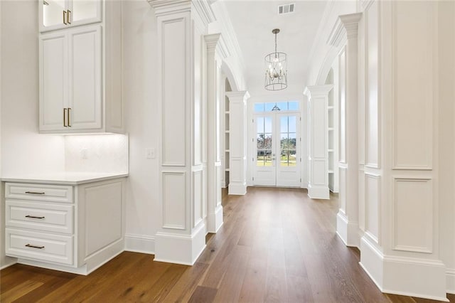 hallway with dark hardwood / wood-style flooring, decorative columns, an inviting chandelier, and crown molding