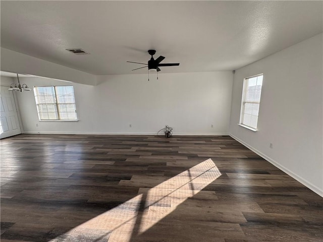 spare room with dark hardwood / wood-style floors, ceiling fan with notable chandelier, and a wealth of natural light