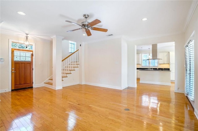 unfurnished living room with ceiling fan with notable chandelier, light wood-type flooring, plenty of natural light, and ornamental molding