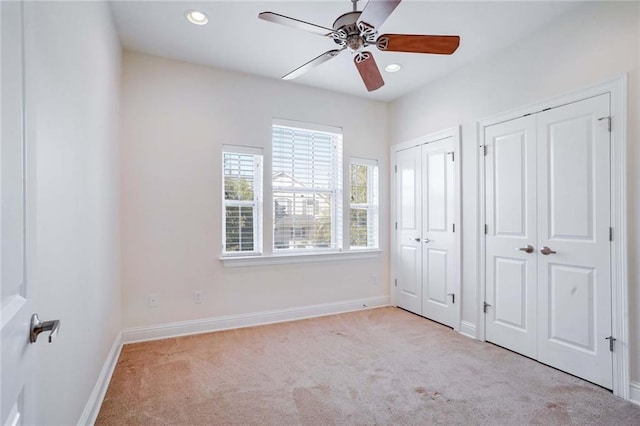 unfurnished bedroom with ceiling fan, light carpet, and multiple closets