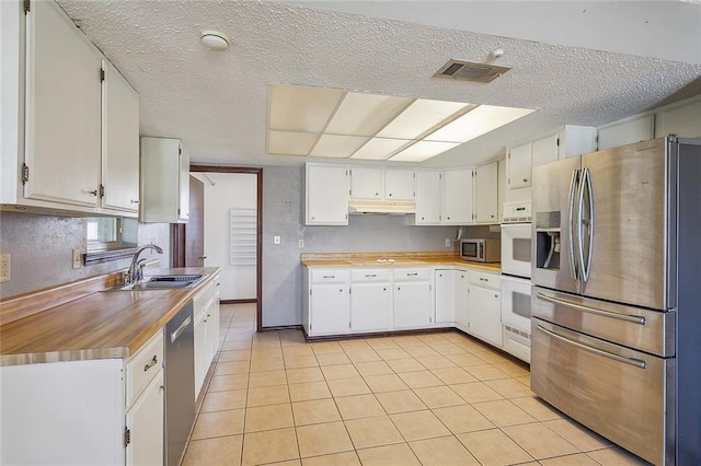 kitchen featuring a textured ceiling, stainless steel appliances, sink, light tile patterned floors, and white cabinetry