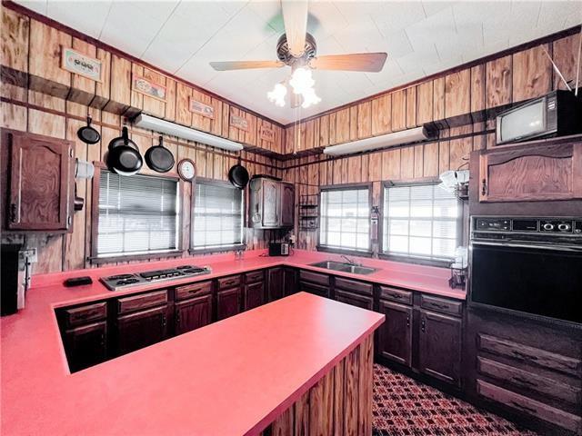 800 Anna St, Lafitte, LA 70067 - kitchen with black oven, wooden walls, stainless steel gas stovetop, light countertops, and a ceiling fan