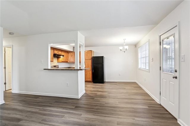 kitchen with kitchen peninsula, black fridge, pendant lighting, an inviting chandelier, and dark hardwood / wood-style floors