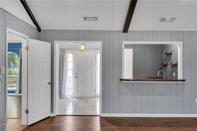 foyer featuring vaulted ceiling with beams, wooden walls, sink, and wood-type flooring