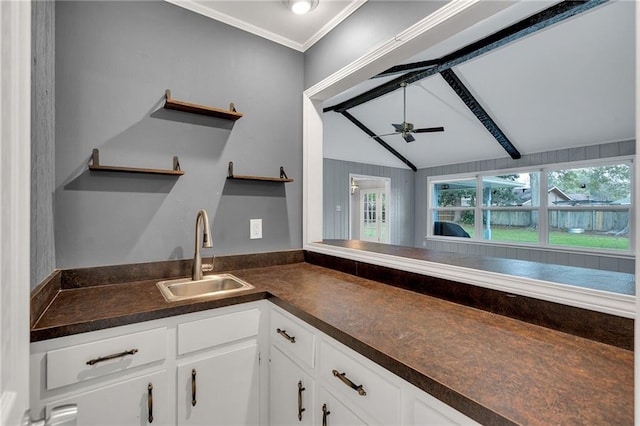 kitchen with ceiling fan, sink, lofted ceiling with beams, white cabinets, and ornamental molding