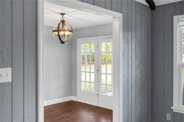 doorway to outside featuring wood walls, dark wood-type flooring, and an inviting chandelier