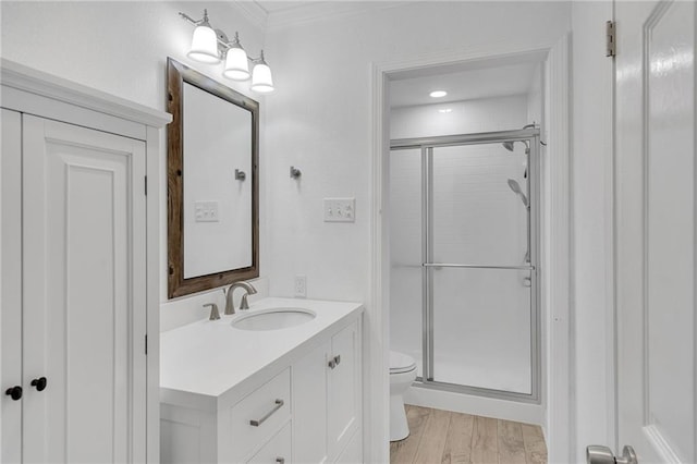 bathroom with vanity, hardwood / wood-style flooring, toilet, ornamental molding, and a shower with shower door