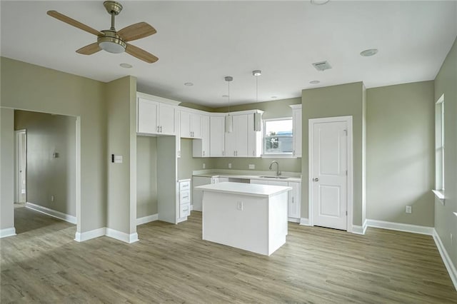 kitchen featuring sink, white cabinetry, a center island, hanging light fixtures, and light hardwood / wood-style floors