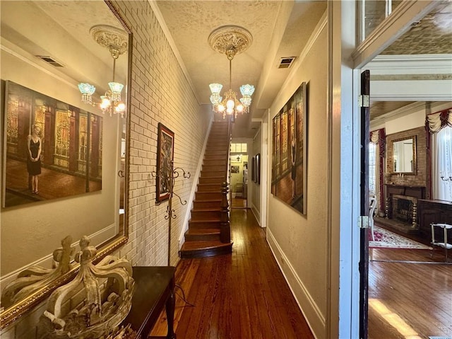 corridor with hardwood / wood-style floors, baseboards, visible vents, crown molding, and a chandelier